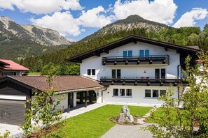 Een terras chalet met twee verdiepingen, met balkon, gelegen aan een verzorgd gazon met een berg op de achtergrond.