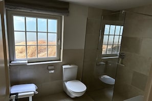 A bathroom with a toilet, a shower, and a window with a view of a field. - Guesthouse of the Brombeerhof (Kampen)