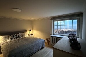 A bedroom with a large bed, a nightstand, a window with a view, and a radiator. - Guesthouse of the Brombeerhof (Kampen)
