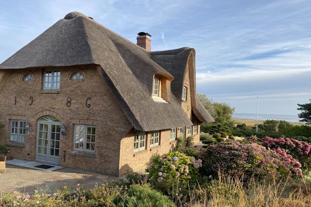 A traditional brick house with a thatched roof, a front door, and a small porch area.