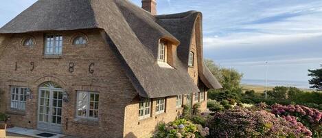 A traditional brick house with a thatched roof, a front door, and a small porch area.