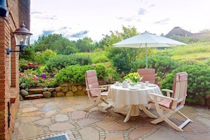 An outdoor patio with a stone floor, a round table, two rocking chairs, and a white umbrella. - Guesthouse of the Brombeerhof (Kampen)