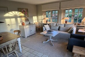 A cozy living room with a sofa, a dining table, and a window with curtains. - Guesthouse of the Brombeerhof (Kampen)