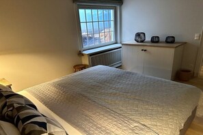 A bedroom with a bed, a window, a radiator, a cabinet, and a bedside table. - Guesthouse of the Brombeerhof (Kampen)