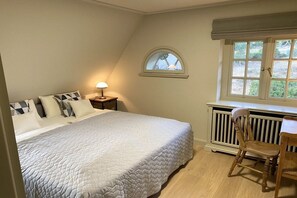 Une chambre à coucher avec un lit, une table de chevet, une chaise, une fenêtre et un radiateur.