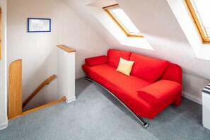 Ein rotes Sofa in einem Zimmer mit schrägen Wänden und Dachfenstern.