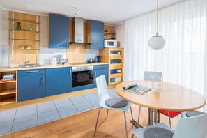 Eine moderne Küche mit blauen Schränken, einer Mikrowelle und einem Essbereich mit rundem Tisch und Stühlen.