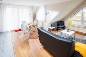 Ein modernes Wohnzimmer mit Essbereich, einem schwarzen Sofa, einem Fernseher und einem Fenster mit Vorhängen.