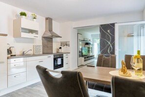 A modern kitchen with white cabinetry, a built-in oven, and a stainless steel range hood. - Holiday apartment with 1 bedroom (Bad Zwischenahn)
