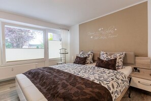 A bedroom with a large bed, a bedside table, a nightstand, and a window with curtains. - Holiday apartment with 1 bedroom (Bad Zwischenahn)