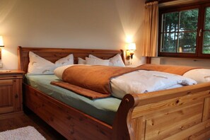 A wooden bed with a headboard, two bedside tables, and a window with curtains. - at the country house Heel (Schwangau)