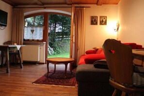 A cozy room with a wooden floor, a red sofa, a small table, and a view of greenery outside. - at the country house Heel (Schwangau)