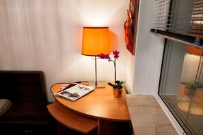 Een hoek van een kamer met een houten tafel, een tijdschrift, een lamp en een bloempot.