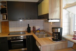 A compact kitchen with a stove, oven, sink, and coffee maker.