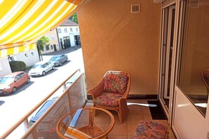 Een balkon met rieten meubilair, een geel zonnescherm en uitzicht op geparkeerde auto's en gebouwen.