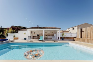 Ein Swimmingpool mit Liegebereich, einer überdachten Terrasse und einem Holzzaun.