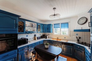 Cozinha com armários azuis, bancada preta e área de refeições com mesa e cadeiras.