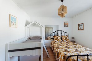 Ein Schlafzimmer mit einem Etagenbett, einer Tagesliege, einem Bett mit floralem Bettbezug, einer Hängeleuchte und zwei gerahmten Bildern an der Wand.