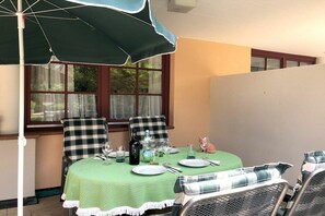 Ein Essbereich mit einem Tisch für zwei Personen, einer grünen Tischdecke und einem karierten Sonnenschirm.