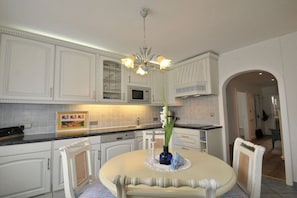 A kitchen with white cabinetry, a round dining table, and a chandelier. - Holiday apartment with 2 bedrooms (Westerland\/Sylt)