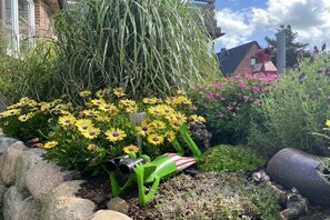 A garden with yellow flowers, green foliage, and a red and white striped object. - Holiday apartment with 2 bedrooms (Westerland\/Sylt)