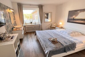 A bedroom with a bed, a bedside table, a chair, a window with curtains, a radiator, and a painting on the wall. - Holiday apartment with 2 bedrooms (Westerland\/Sylt)