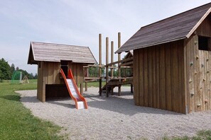 Ein Spielplatz mit Rutsche und Kletterwand, umgeben von Holzkonstruktionen.