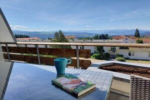 Un balcó amb vista a una cadena de muntanyes, un llibre i una tassa blava sobre una taula.