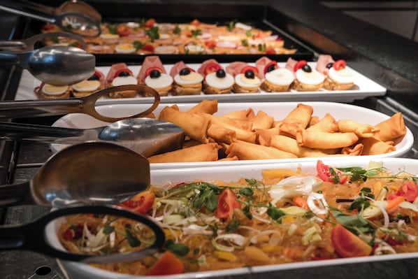 Un buffet proposant une variété de plats, notamment des rouleaux de printemps, des salades et des desserts.
