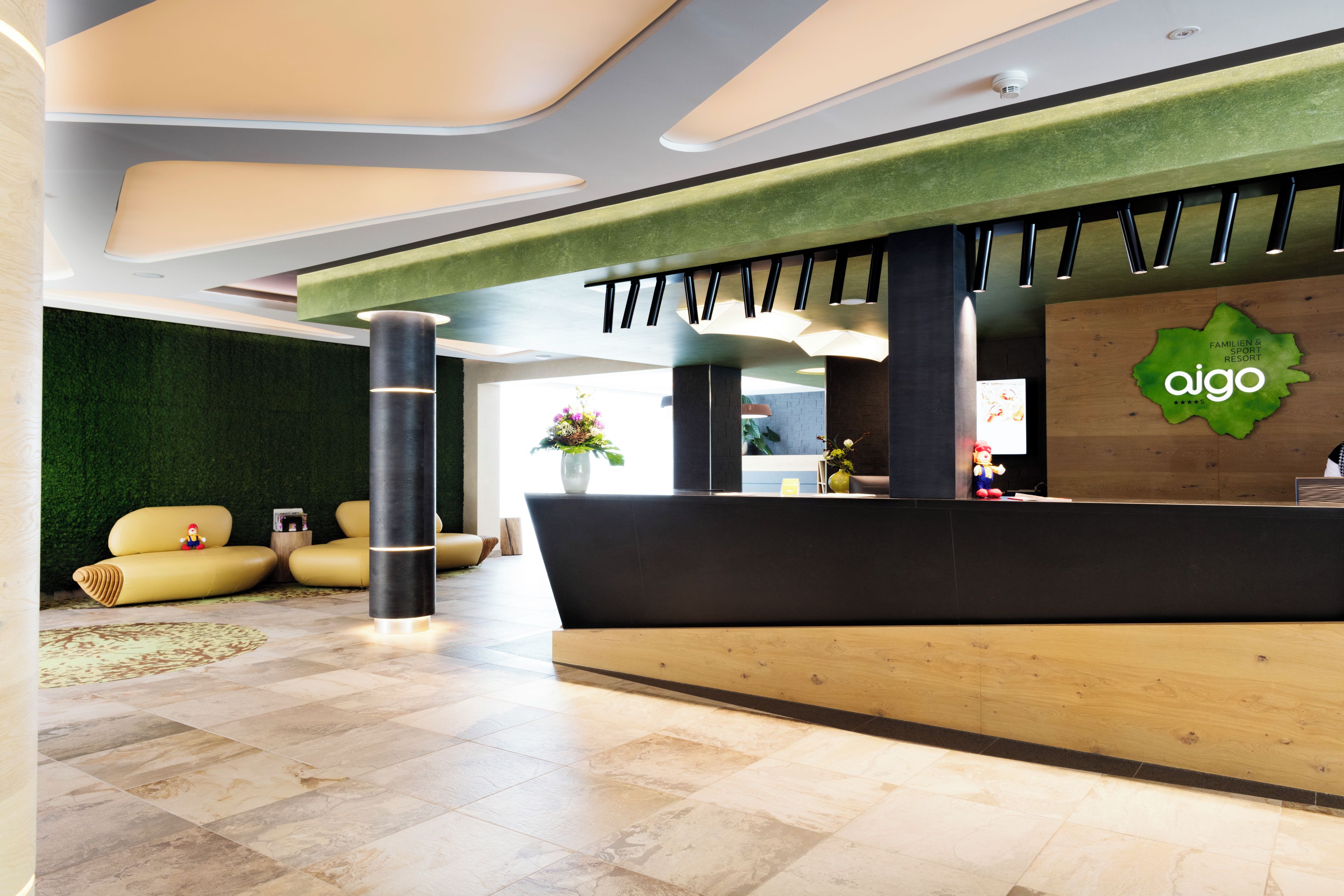 A modern reception area with a green wall, a reception desk, and a seating area with yellow sofas.