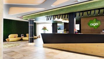 A modern reception area with a green wall, a reception desk, and a seating area with yellow sofas.