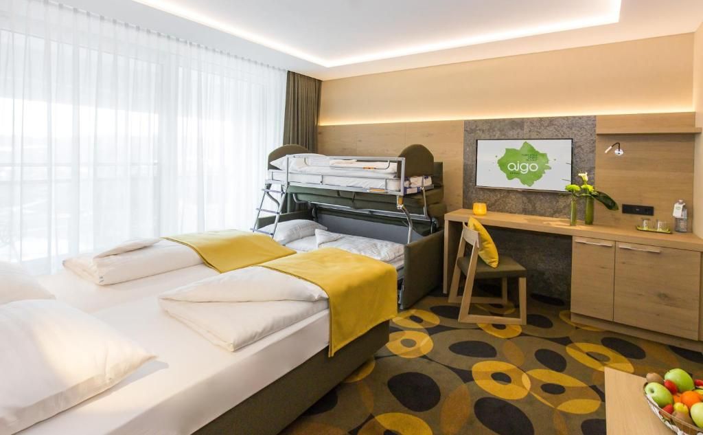 Habitación de hotel con literas, un escritorio, una silla, una mesita con un florero y una cesta de frutas.