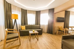 Une chambre d’hôtel moderne, équipée d’un canapé, d’une petite table, d’une lampe et d’un téléviseur.