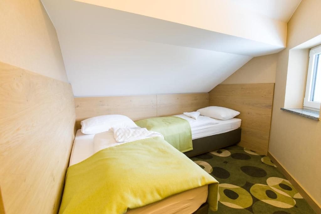 A small, triangular room with two beds, a window, and a patterned carpet.