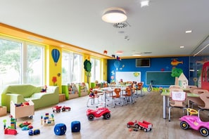 Une salle de jeux pour enfants aux couleurs vives, avec des tables, des chaises et divers jouets.