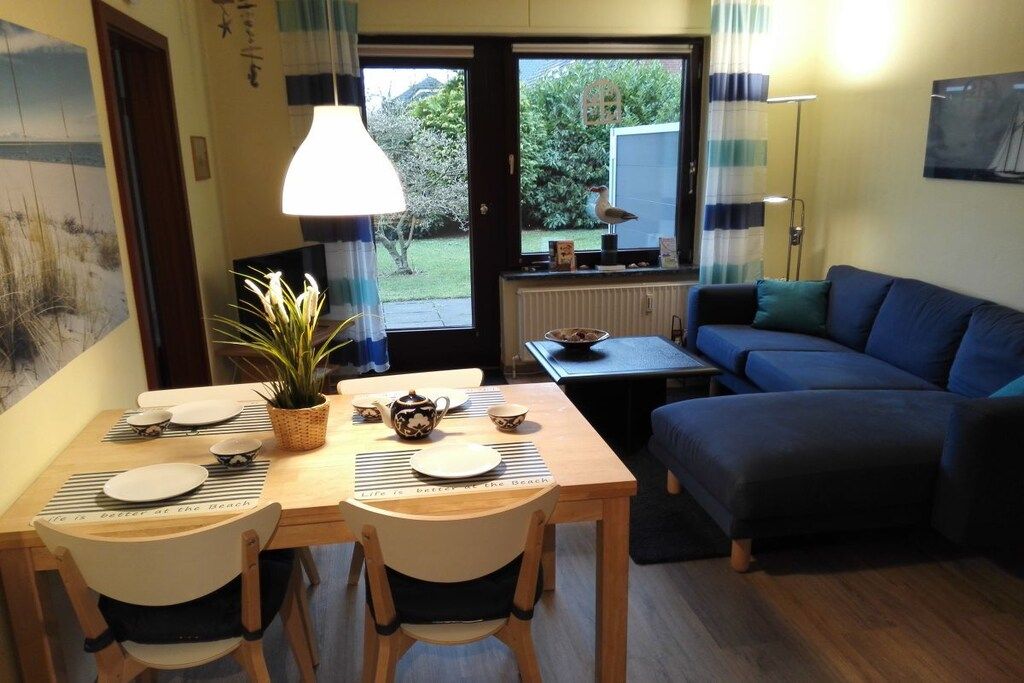 Un coin repas avec une table dressée pour deux personnes, un canapé bleu et une vue sur l’extérieur.