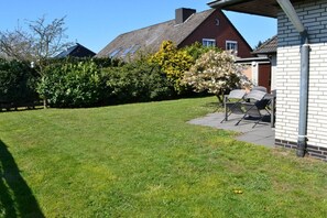 Ein gepflegter Rasen mit einer Terrassenfläche, Gartenmöbeln und einem Backsteinhaus.