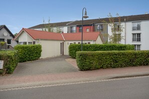 A residential building with a red-tiled roof, a paved driveway, and a well-maintained hedge. - Bungalow 'Haus S 41 Paulchen' with Private Terrace, Private Garden and Wi-Fi (Röbel/Müritz)