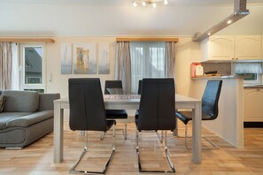 A modern living room with a dining table, chairs, a sofa, and a kitchen area. - Bungalow 'Haus S 41 Paulchen' with Private Terrace, Private Garden and Wi-Fi (Röbel/Müritz)