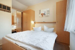 A bedroom with a bed, a wooden wardrobe, a painting on the wall, and a window with curtains. - Bungalow 'Haus S 41 Paulchen' with Private Terrace, Private Garden and Wi-Fi (Röbel/Müritz)