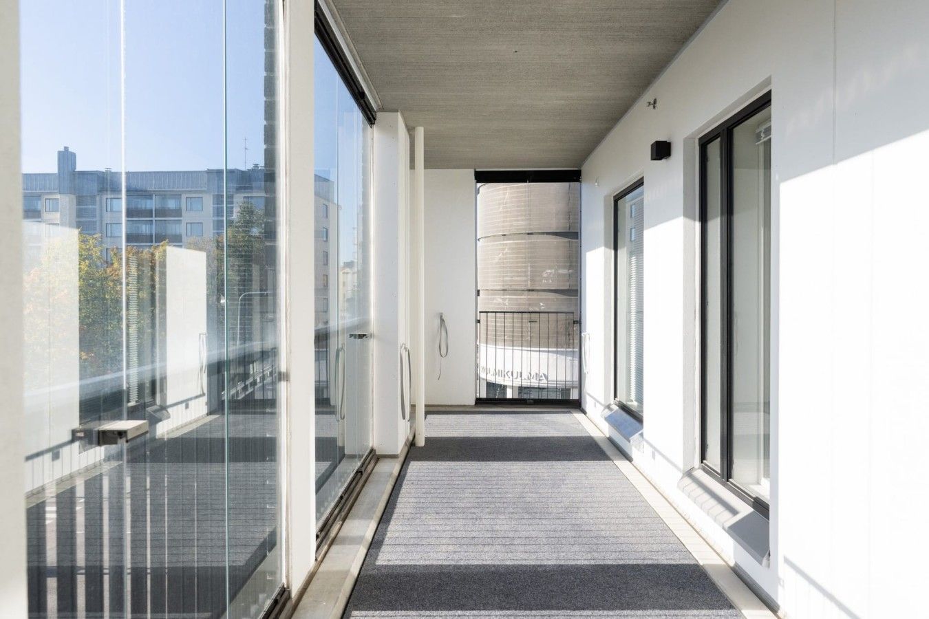 A corridor with glass doors leading to a balcony, a metal gate, and a view of buildings in the distance.