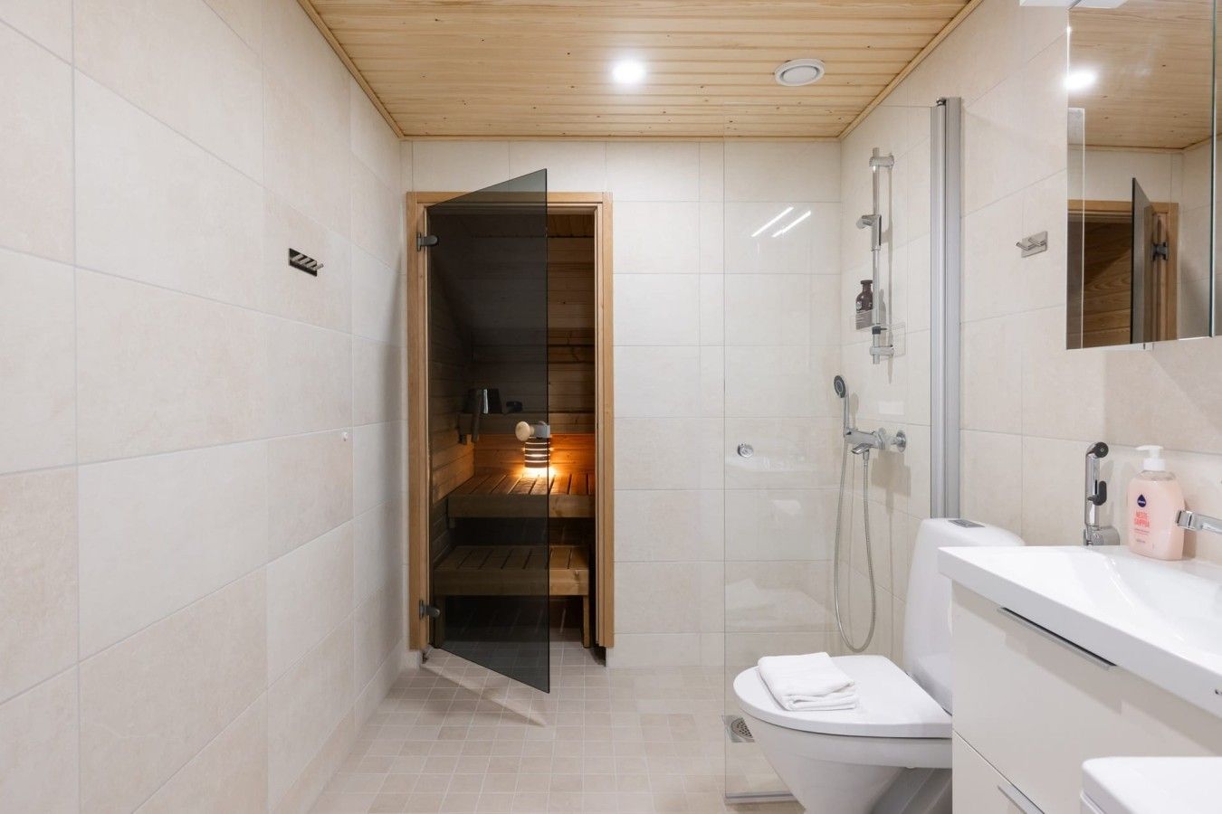 Un bagno moderno con sauna in vetro, doccia e lavandino bianco con specchio.