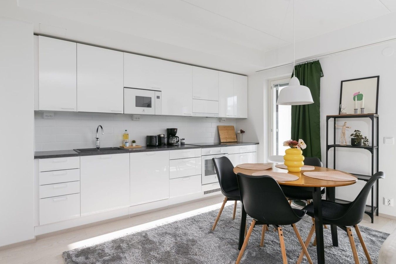 A modern kitchen with white cabinets, a dining table with chairs, and a coffee machine.