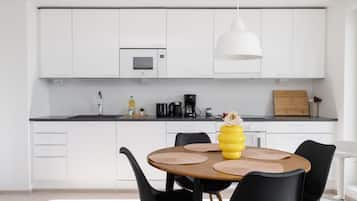 Una cocina moderna con armarios blancos, una mesa redonda de comedor con sillas negras y un jarrón amarillo con una flor.