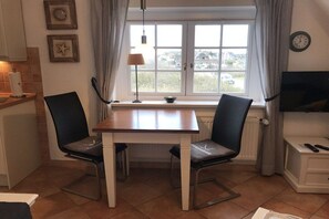 Ein Essbereich mit Tisch und Stühlen, einem fenster mit Vorhängen, einer Lampe und einer Uhr an der Wand.