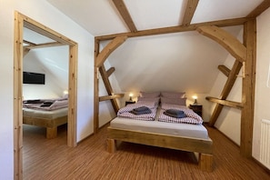 A loft bedroom with a wooden ceiling structure, a bed with checkered bedding, bedside lamps, and a mirror on the wall. - Chalet "Zur Werraquelle" (Masserberg)