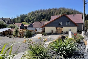 A residential area with houses, a gravel driveway, and a forested hill in the background. - Chalet "Zur Werraquelle" (Masserberg)