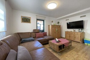 Ein Wohnzimmer mit einem braunen Ledersofa, einem Holztisch, einem Fernseher und einem Schrank.