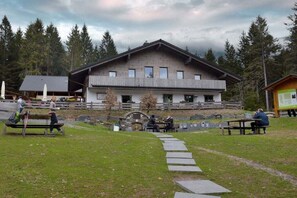 Un bâtiment doté d’une façade en pierre, d’une terrasse en bois et d’un chemin en pierre menant à un espace avec des bancs.