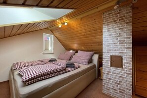 Ein Einzelbett mit karierter Bettwäsche in einem Zimmer mit geneigter Decke und Backsteinwand.